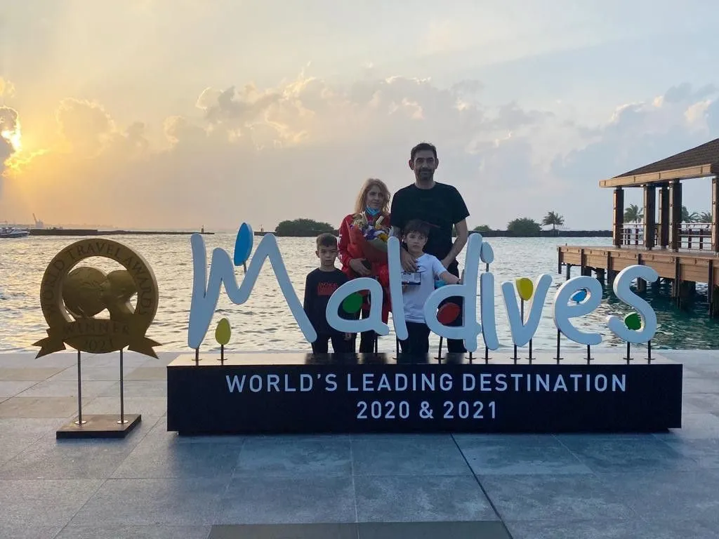 Tourists near visit Maldives logo placed outside of Velana International Airport.